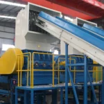 The image depicts a wet plastic grinding machine used in the recycling industry to process plastic waste. This type of machinery combines the steps of washing and grinding plastic materials to prepare them for further processing, such as pelletizing or compounding. The machine includes a large hopper for loading the waste plastic, a water injection system to aid in the breakdown and cleaning of materials, and a conveyor system that transports the plastic through various stages of grinding and washing. The integration of water not only improves the efficiency of the grinding process but also reduces dust and other airborne contaminants, making it an environmentally friendly solution for plastic recycling facilities.