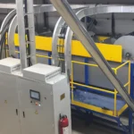 Intérieur d'une installation de recyclage industriel comprenant une ligne de lavage et de recyclage de films PP et PE broyés. L'équipement est peint en jaune vif et bleu, ce qui améliore la visibilité. Il comprend divers convoyeurs, trémies et un tambour rotatif cylindrique, tous intégrés dans une configuration compacte et efficace. Des garde-corps de sécurité et un extincteur sont visibles, soulignant les mesures de sécurité en place.