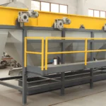 un réservoir de séparation industriel à flotteur-évier dans une usine de fabrication. Le réservoir est allongé, avec un dessus jaune vif et des composants structurels gris. Plusieurs moteurs électriques montés sur le dessus du réservoir suggèrent sa fonctionnalité opérationnelle. La structure est soutenue par un cadre métallique robuste gris foncé avec des garde-corps de sécurité peints en jaune. L'arrière-plan de la photo indique un environnement industriel avec diverses machines et outils dispersés un peu partout. Le sol est en béton et la lumière naturelle illumine l'espace à travers des fenêtres visibles au sommet.