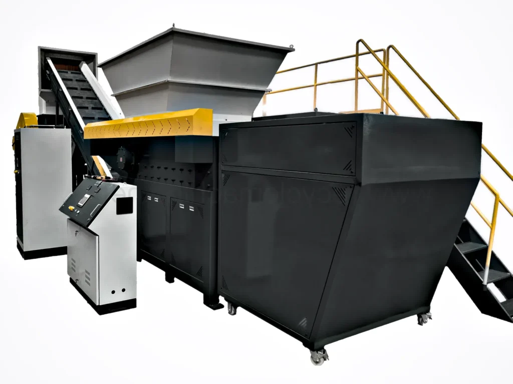 A complete waste shredding station with an inclined conveyor belt, a large industrial shredder, an operator control panel, and a large black mobile bin for collecting the shredded output.