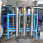 eine thermische Trocknungsmaschine, die Teil eines industriellen Systems ist, das zum Trocknen von Materialien durch Hitze entwickelt wurde. Der Aufbau umfasst eine Reihe von Metallrohren und -zylindern, wahrscheinlich zum Transport von Materialien und heißer Luft. Mehrere im Bild sichtbare Motoren und mechanische Komponenten lassen darauf schließen, dass dieses System mit einer Kombination aus Hitze und mechanischer Bewegung arbeitet, um eine effiziente Trocknung zu erreichen. Die Verwendung von rostfreiem Stahl und die robuste Struktur weisen darauf hin, dass es für Langlebigkeit und hohe Leistung in industriellen Umgebungen gebaut ist.