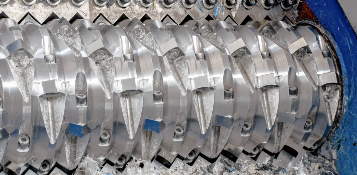 A close-up view of an industrial shredder's rotating shaft with sharp, heavy-duty cutting blades for the size reduction of waste materials.