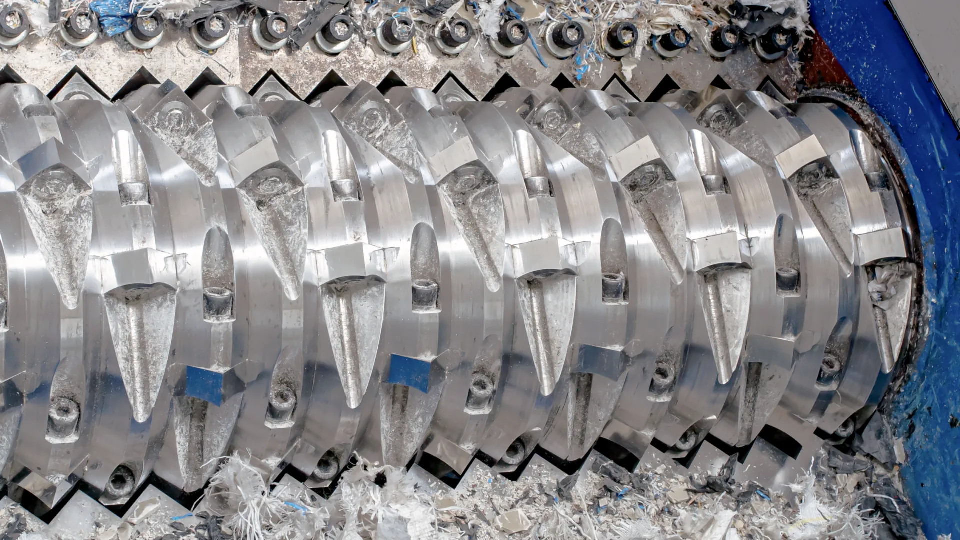A close-up view of an industrial shredder's rotating shaft with sharp, heavy-duty cutting blades for the size reduction of waste materials.